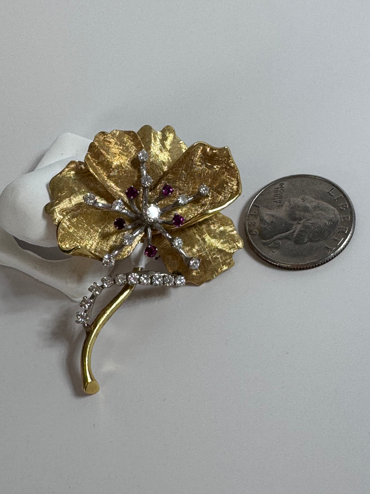 Gold flower-shaped brooch with gemstones on a white background, next to a quarter for scale.