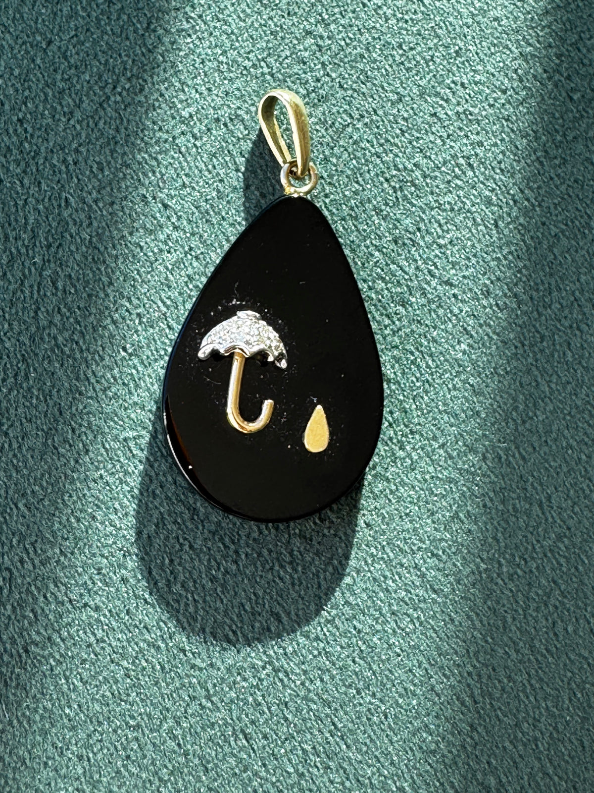Black teardrop-shaped pendant with gold accents on a green textured surface