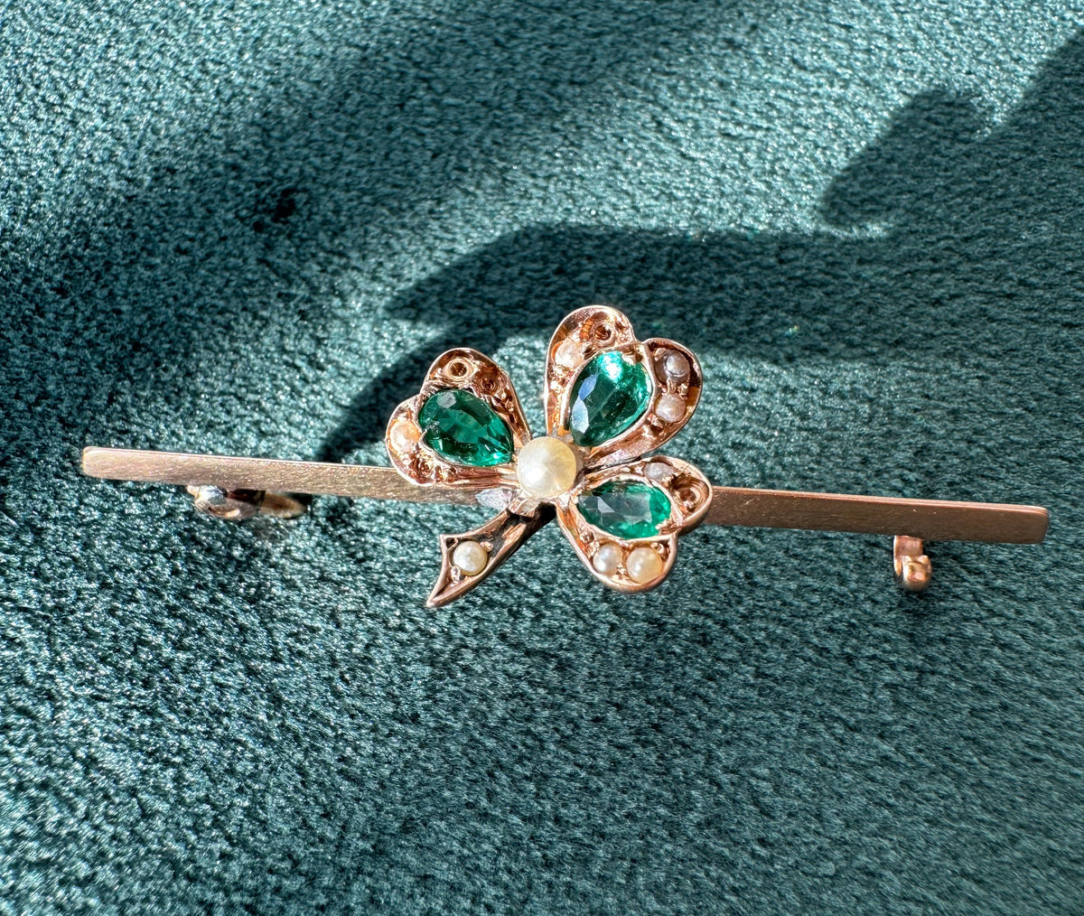 Gold brooch with green gemstones on a textured green background