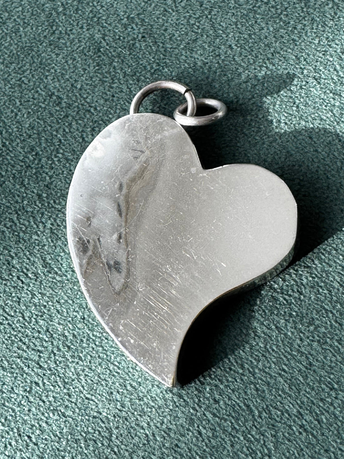 Heart-shaped silver pendant on a textured green surface