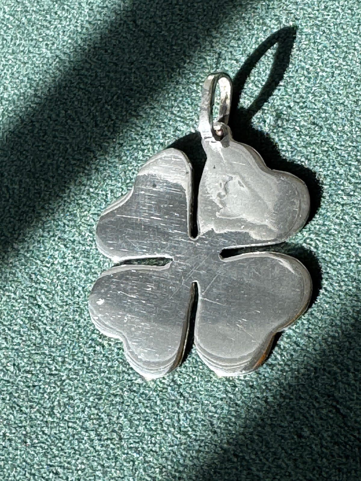 Silver four-leaf clover pendant on a textured green surface