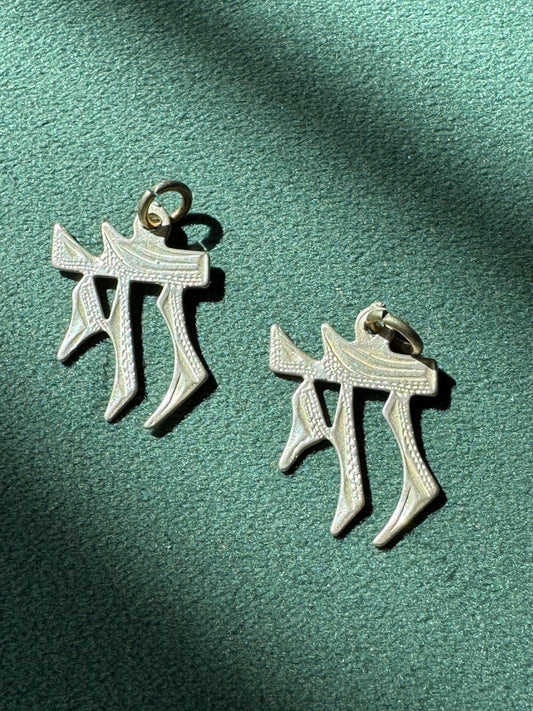 Two silver pendants on a green fabric background