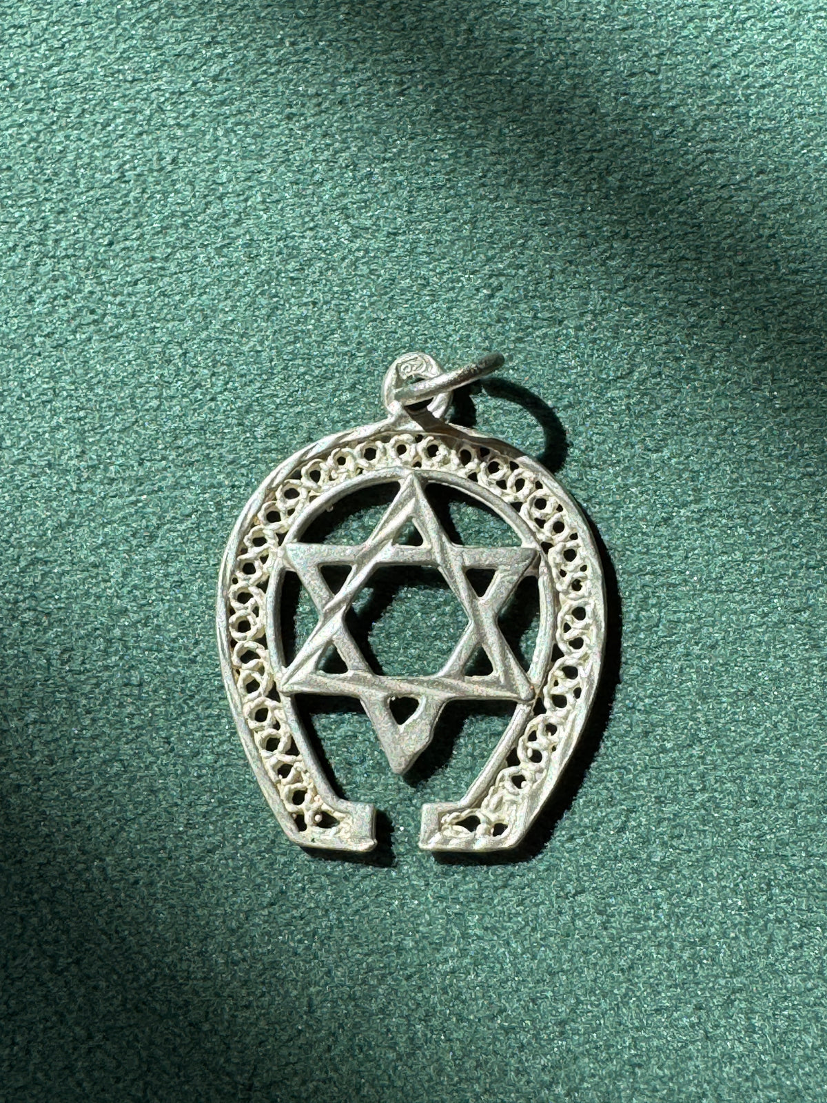Silver pendant with Star of David and horseshoe design on a green background