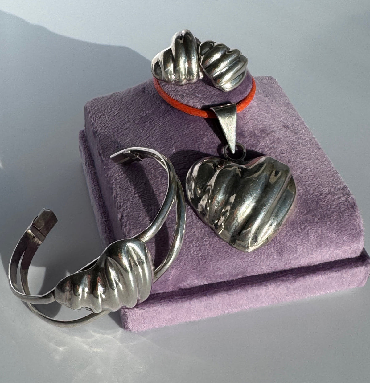 Sterling silver puffy heart jewelry set including cuff bracelet, stud earrings, and pendant with orange cord